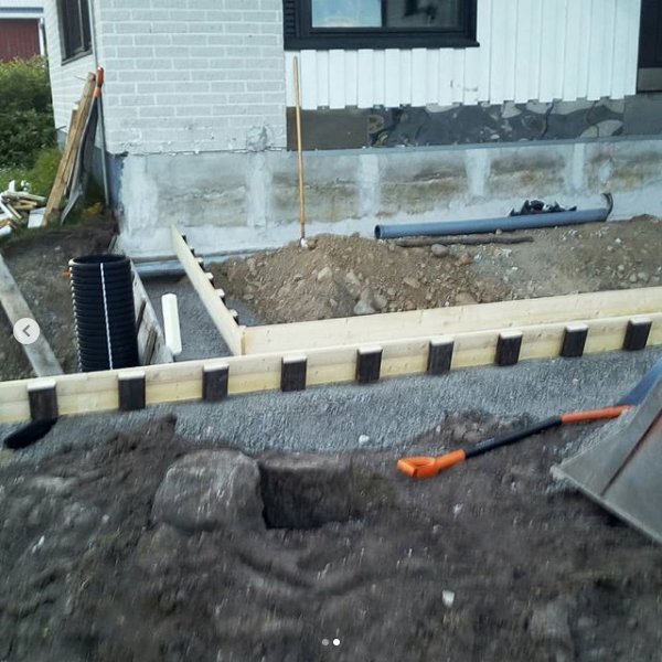 Renovering av altan pågår med synligt grävda fundament och byggmaterial vid en husgrund.