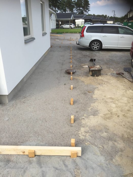 Förberedelse av yta för markbetong med träform och nedslagna pålar vid husvägg, verktyg synliga.