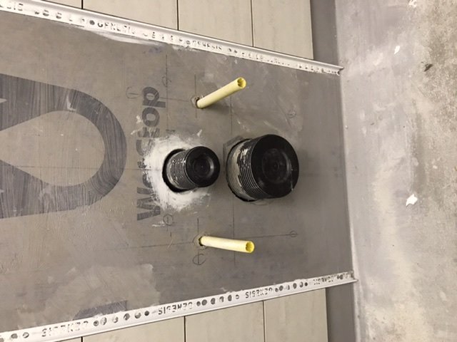 Industriella svarta rör genom en fixturvägg med måttmarkeringar och tätningsmaterial.