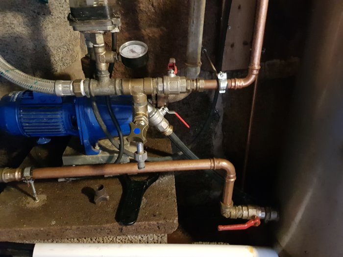 Vattenpump och kopparledningar med kranar för ett anpassat vattensystem i växthus.