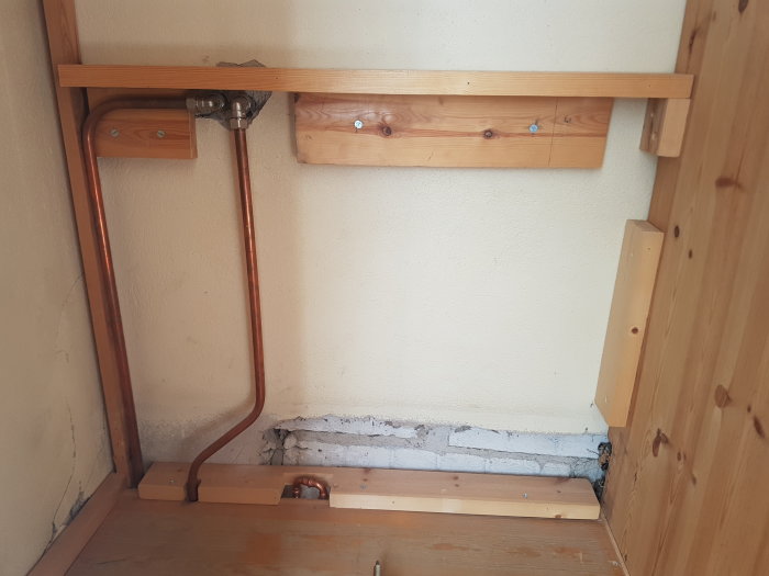 Gamla avstängda rör i en garderob, omgivna av träpaneler, med nya kopparrör synliga.