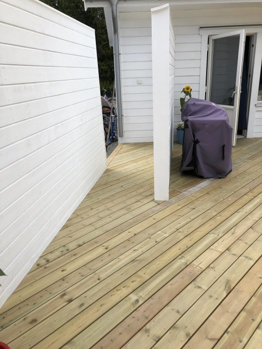 Nybyggd träaltan med vita sidoväggar och plats för utemöbler nära husentré.