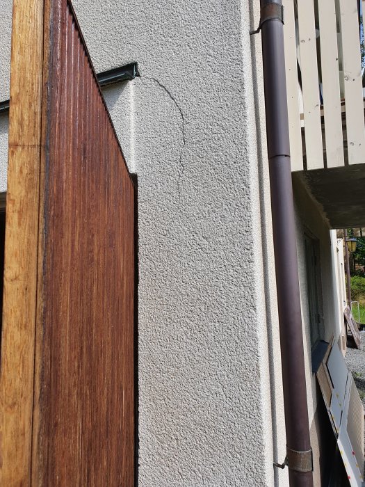 Vanhan talon ulkoseinä jossa on halkeama rappauksessa; puupaneeli ja syöksytorvi näkyvissä, mahdollinen korjaustarve.