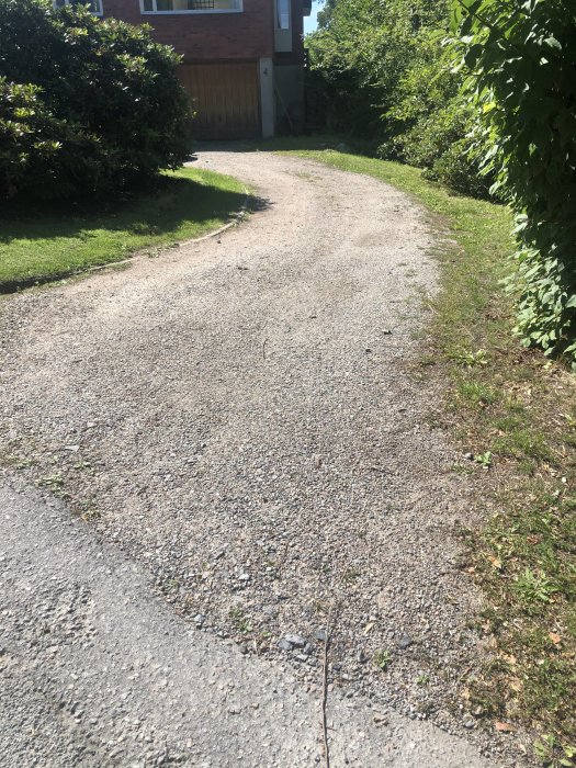 Grusad uppfart med ojämna kanter och viss vegetation intill, synligt slitage från 60-talet, kräver underhåll.