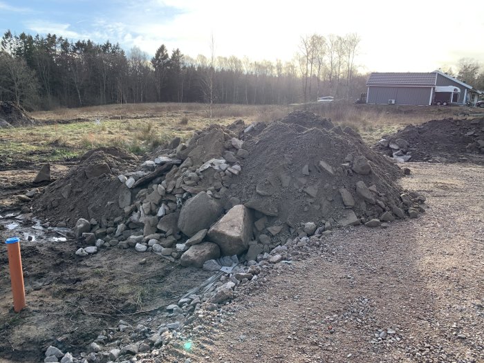 Högar av grus och sten på en byggplats med tydliga tecken på markarbete under våren.