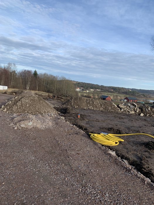 Markarbeten pågår med synliga högar av grus och jord samt en gul slang på ett bygge under våren.