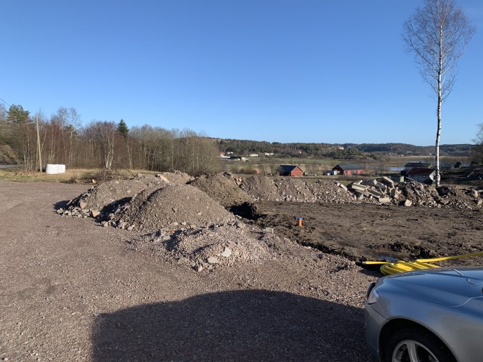 Pågående markarbete med högar av grus och jord, betongrester, med landskap och klarblå himmel i bakgrunden.