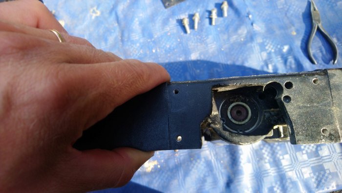 Hand som håller en del av aluminiumramen med synliga lagerhållare och en demonterad lagerenhet med verktyg i bakgrunden.