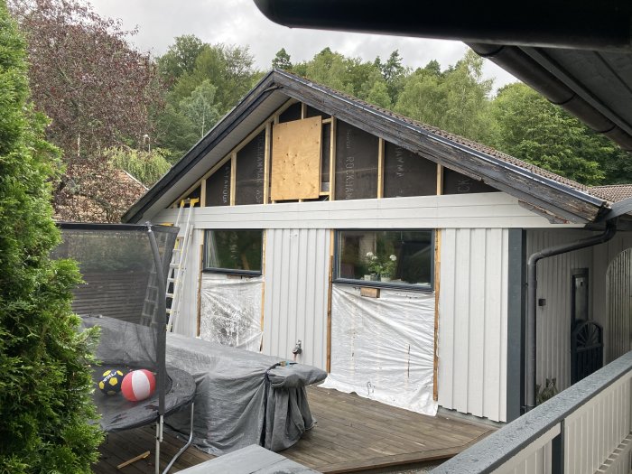 Halvfärdigt hus med ny spikad panel och skyddsplast under ett grått och molnigt himmel.
