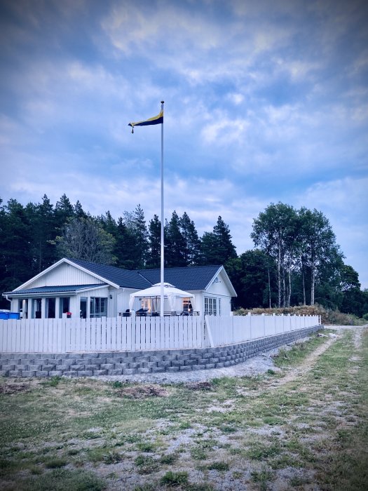 Vit trästaket under uppbyggnad vid en villa med en svensk flagga på en flaggstång.