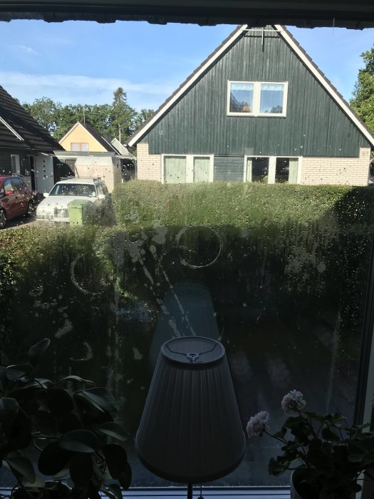 Utsikt genom nytt fönster med kvarvarande vattendroppar på glaset efter regn, utsikt mot parkerad bil och hus.