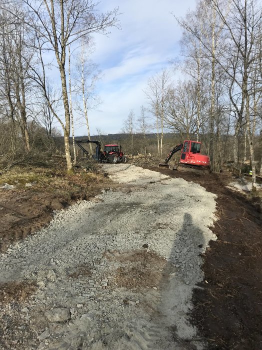 Arbetsplats utomhus med röd grävmaskin och traktor vid bygget av en ny garagegrund.