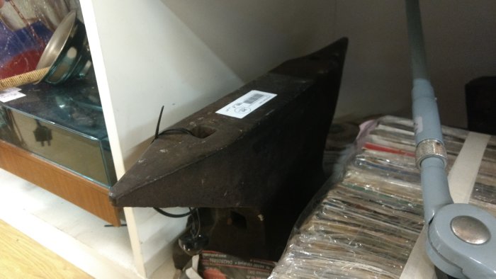 Gammalt rostigt strykjärn lämnat i ett rörigt förrådsutrymme med speglar och plaströr.