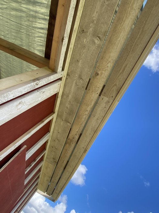 Del av träkonstruktion för hus med vindskivor och läkt under en blå himmel.
