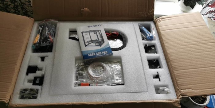 Ny 3D-skrivare i kartong med komponenter och installationsmanual synliga.