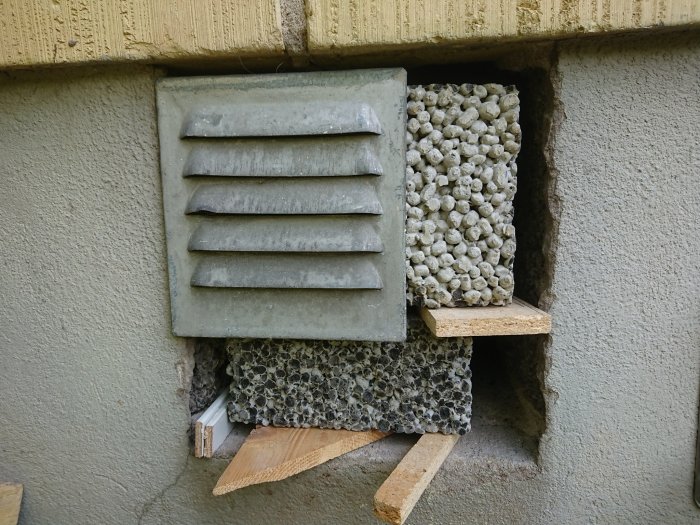 Monteringsförberedelser med en ventilstensblock nära en vägg, stödd på träbitar, med en glipa vid ramen och hörnet.