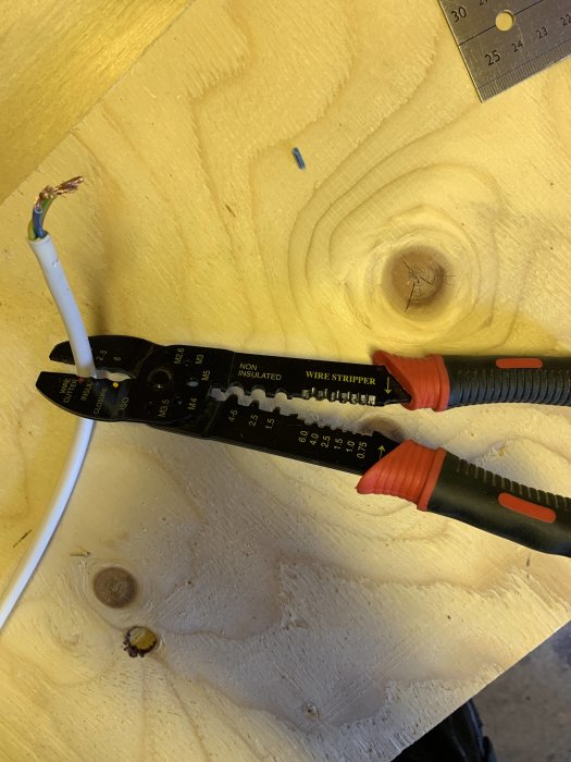 Avskalad elkabel med exponerade ledare bredvid en kabelskalare och en linjal på en träyta.