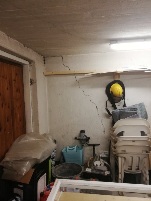 Stor spricka som sträcker sig från ett garage- eller källartak ner längs en betongvägg, med förvarade föremål nedanför.
