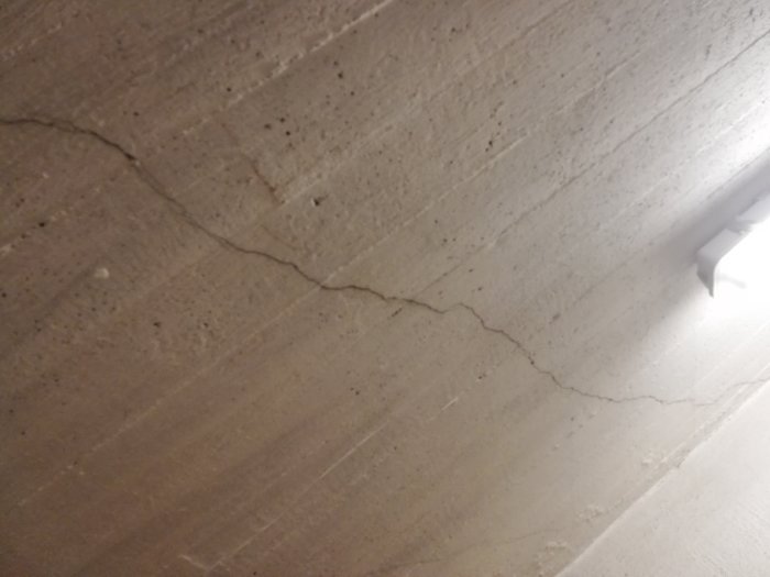 Spricka i grå betongvägg i garage, under belysning, möjlig strukturbekymmer.