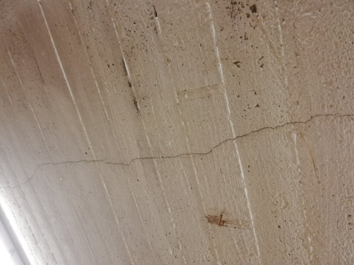 En tunn, lång spricka i ett betongtak, med synliga linjer och mindre defekter i materialet.