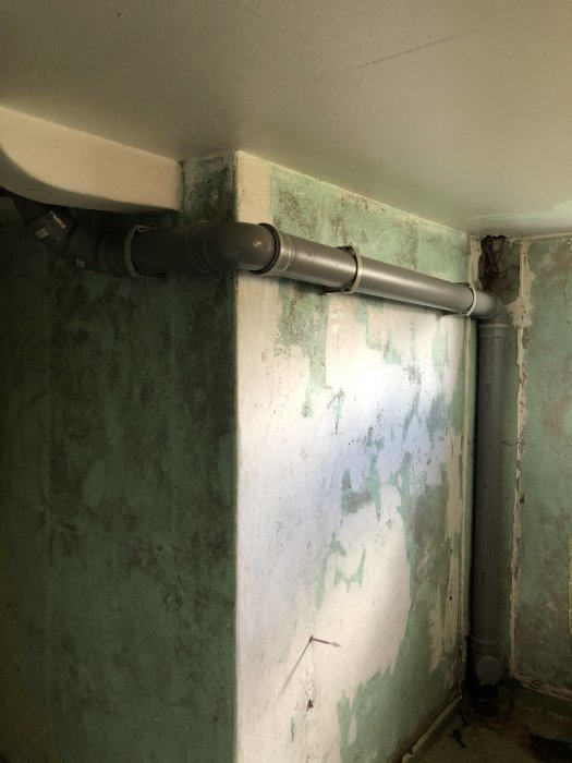 Nylagt grått avloppsrör längs väggen i ett rum under renovering med synliga isoleringsmaterial och rörinstallationer.