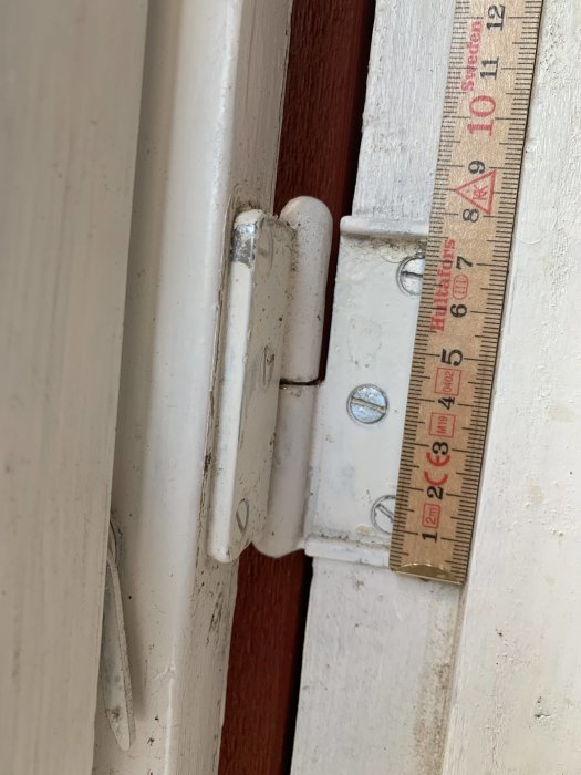 Gångjärn på vit dörr mäts med trälinjal, söker liknande udda modell.