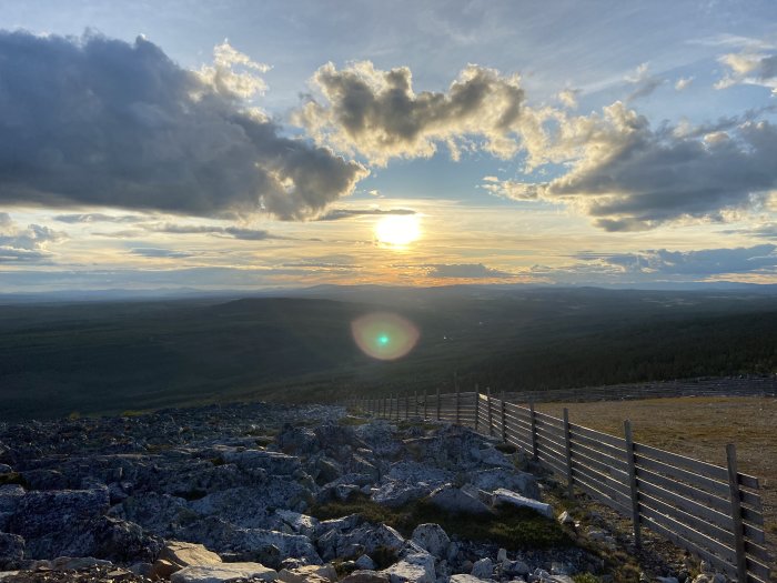 Solnedgång över kuperat landskap med stenig terräng och trästaket.