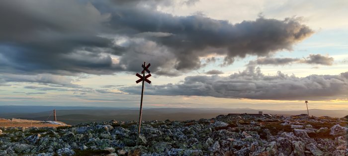 Vy över fjällterräng vid solnedgång med dramatisk molnhimmel och vandringsledsmarkering.