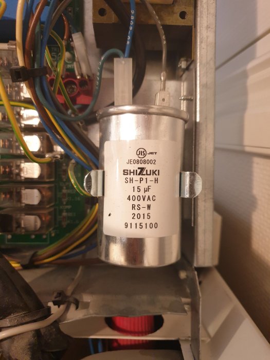 Närbild av en ny rosa kondensator märkt "SHIZUKI 15 µF 400VAC" monterad i en elektrisk anordning.