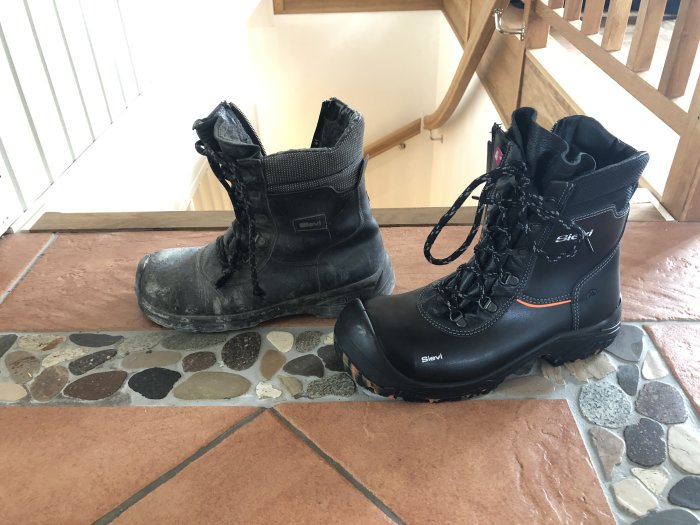 En gammal sliten Sievi-arbetssko bredvid en ny Sievi-arbetssko på ett stengolv.