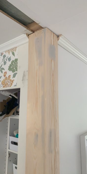 Träpelare i hörn där vägg är borttagen med avslutad taklist och synlig plankända som möter från taket.