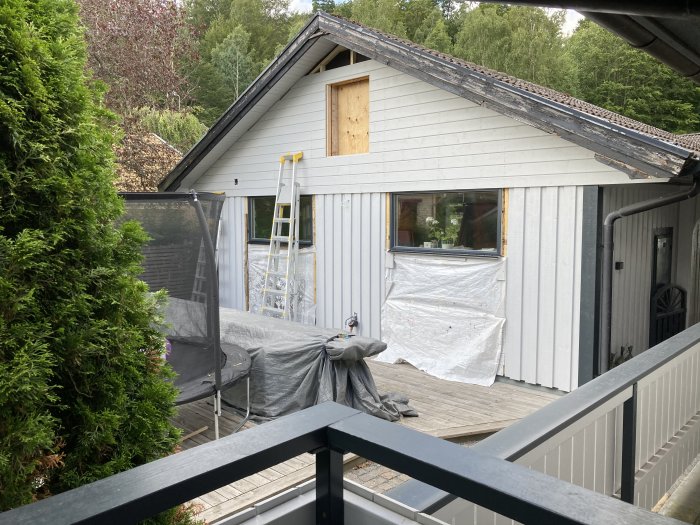 Renovering av husfasad med vit panel och en stegstege, täckta möbler och byggmaterial.