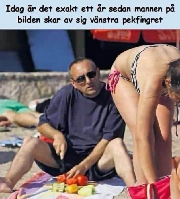 Man sitter på strand och förbereder mat medan en annan person böjer sig ner framför honom.