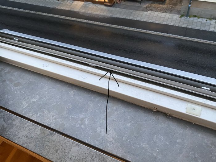 Fönsterskena med en synlig böjning i mitten som hindrar stängning, fotograferad inifrån ett rum.
