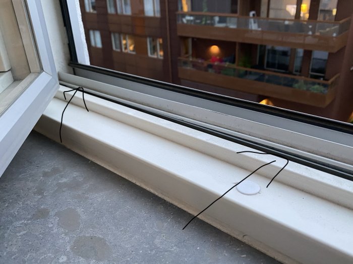 Böjd skena i fönster som hindrar stängning, med utsikt mot byggnad i bakgrunden.