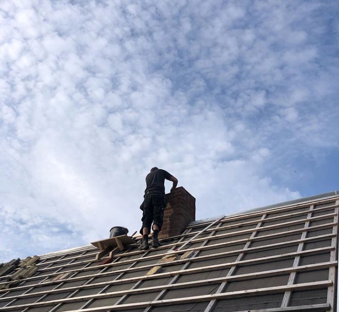 Person som arbetar på en ny murad skorsten på ett hustak mot molnig himmel.