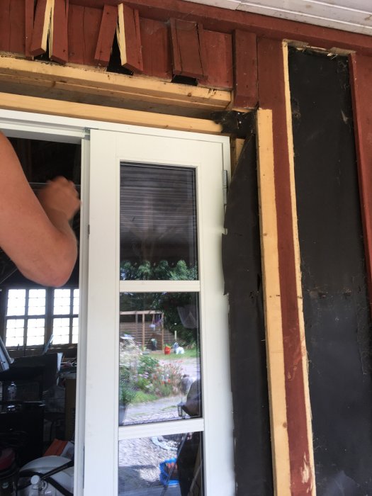 Fasaden runt en nyinstallerad dörr på logen med avlägsnad panel och exponerad isolering klart för renovering.