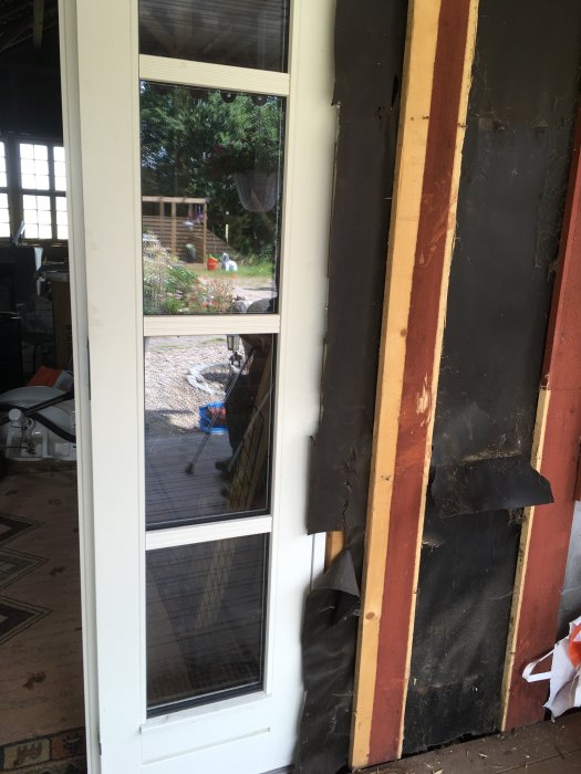 Nyinstallerad vit ytterdörr med otillräcklig eller skadad träpanel och isolering runtom, synlig ventilation och trädgård bakom.