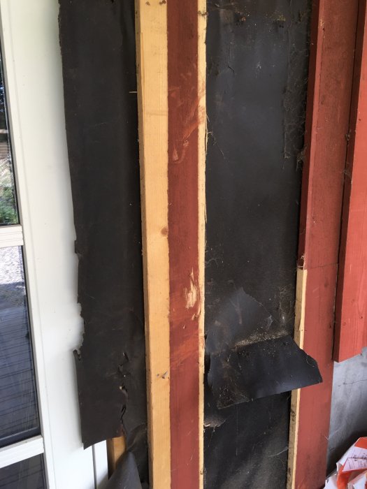 Närbild på en fasad under renovering, visar nya och gamla paneler med isolering och spiderväv.