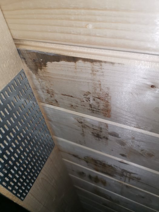 Missfärgningar och mörka fläckar på trävirke i ett vindutrymme, eventuella tecken på fuktskador.