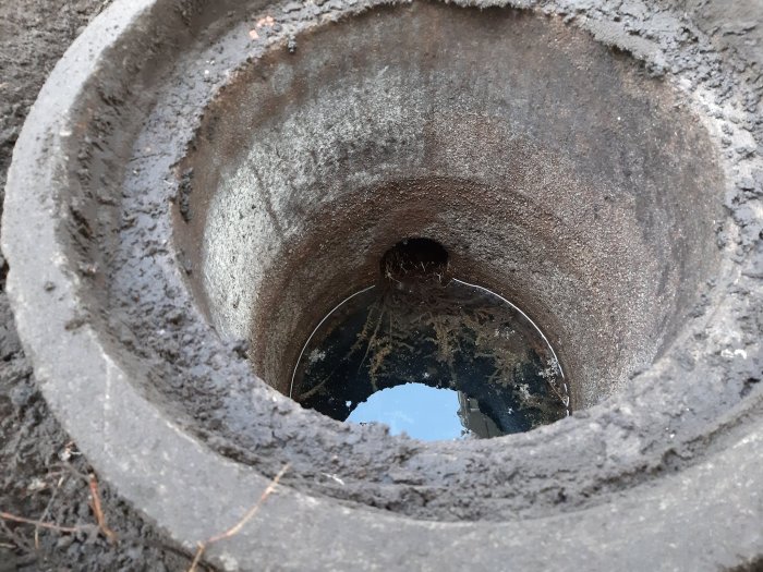 En öppen gammal brunnsring och ett mörkt hål i marken, täckt av smuts och spindelväv.