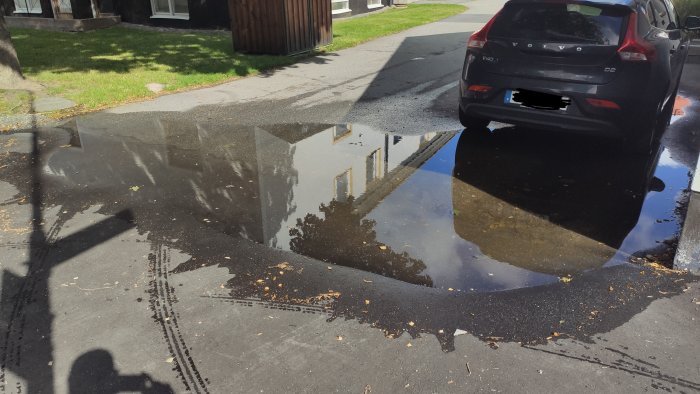 Vattenpöl på en nyhöjd asfaltsyta vid fastighet som skapar potentiell översvämning.