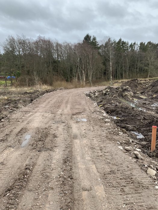 Grusad vägbygge med avmärkta pinnar där ett garage/verkstad planeras, med skog i bakgrunden.