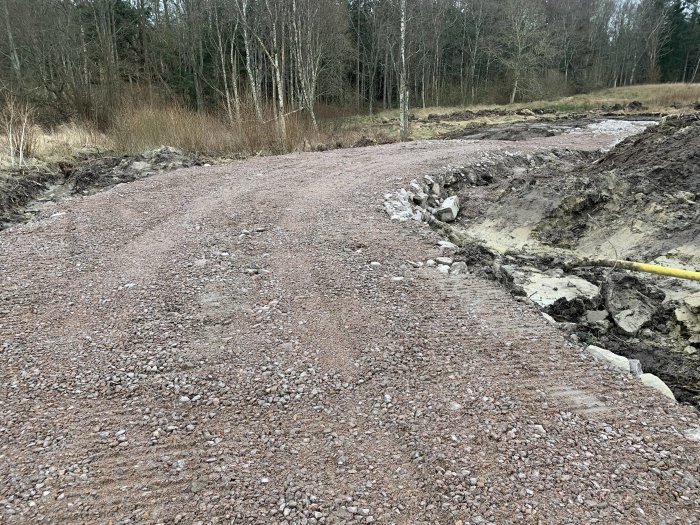 Grusad väg under konstruktion med nedgrävda rör längs den framtida garageinfarten och verkstadsplats markerad med pinnar.