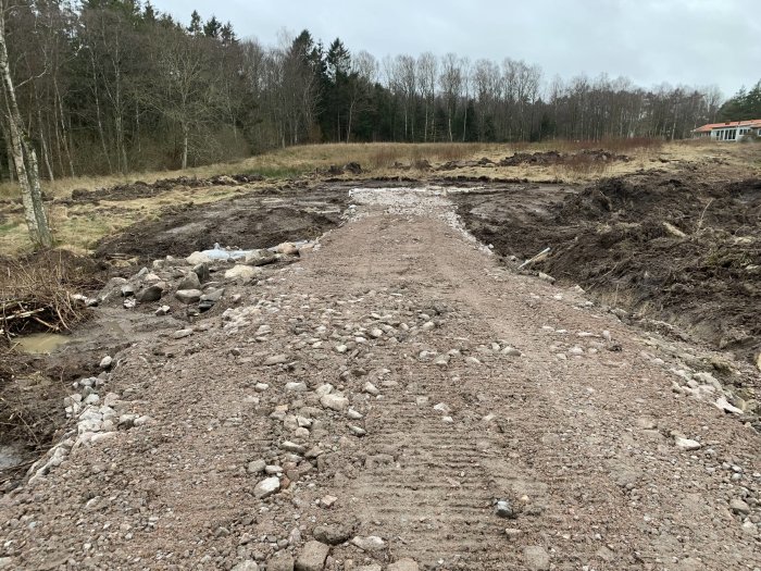 Vägbygge med grusväg och rörlagd dränering i förberedelse för garage och verkstad, markerat med pinnar.