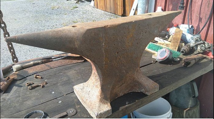 Gammalt rostigt städ från 1800-talet av märket Söderfors på ett träbord, omgivet av verktyg.