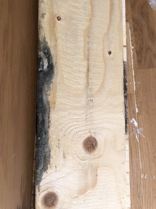 Parkettdel ligger upp och ner med synliga träådringar och en stor svart fläck vid ena kanten.