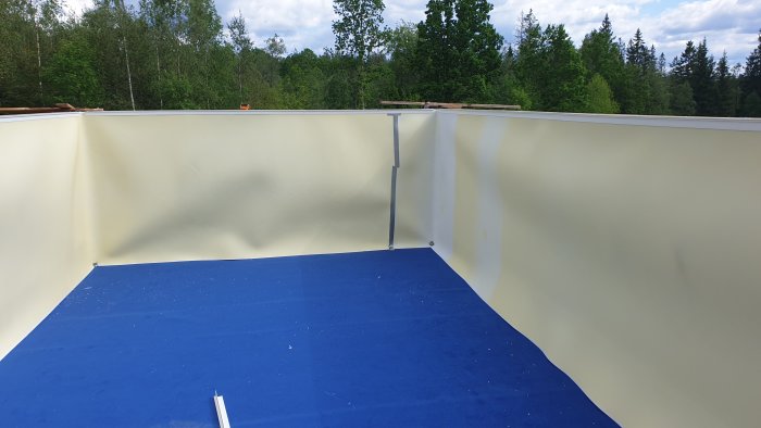 Innertaket i en pool med lantbruksplywood och blå poolmatta på botten, väggar av poolcellplast.
