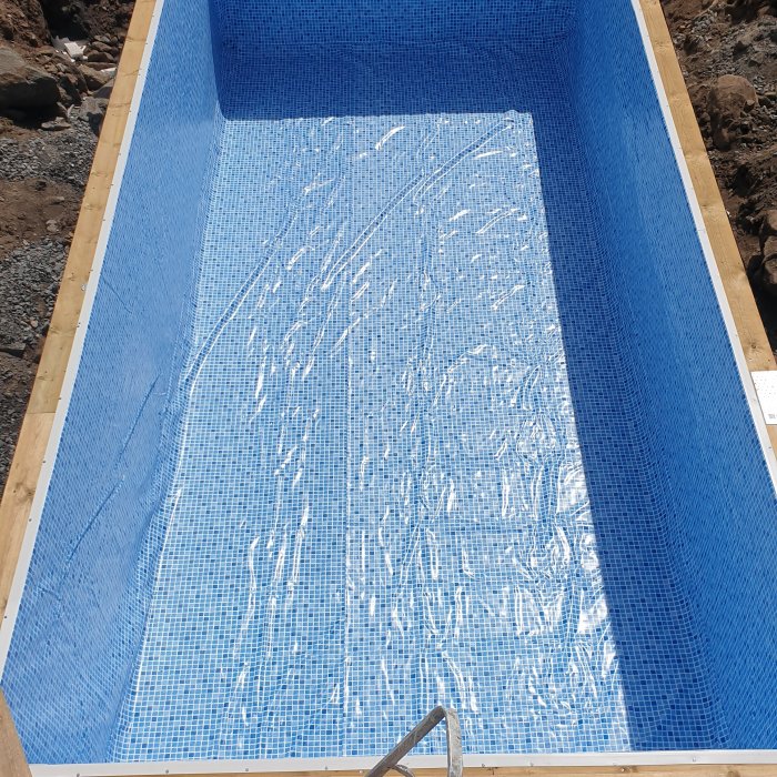 Poolkonstruktion i grävd grop med en nyligen installerad blå poolliner som ligger i veck på poolens botten.