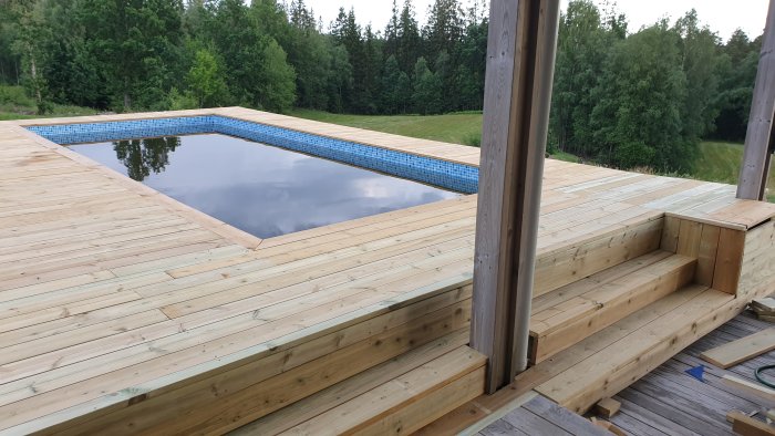 Nybyggd trall runt en pool med spegelblank yta och reflexioner av skogen i bakgrunden.